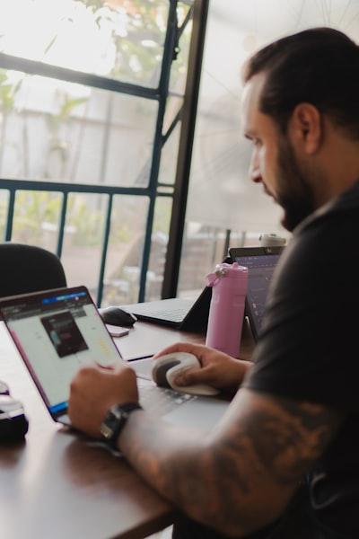 Man working on a laptop with a pink water bottle nearby