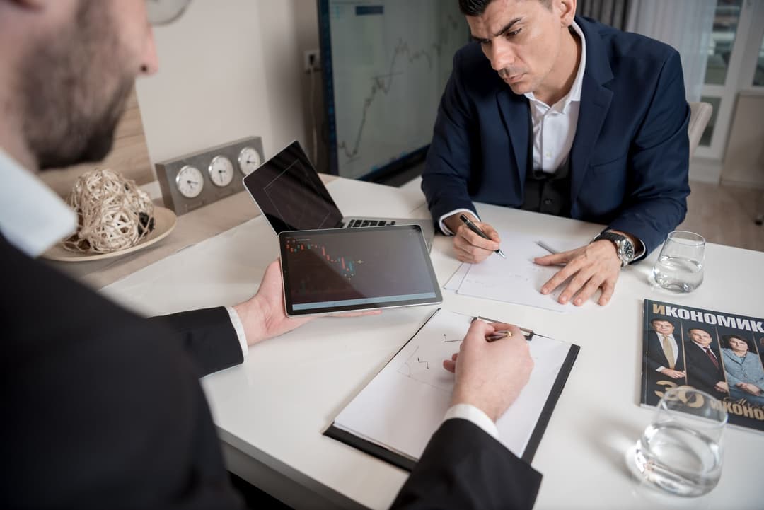 Business owner and finance manager reviewing transaction details behind a monthly financial result
